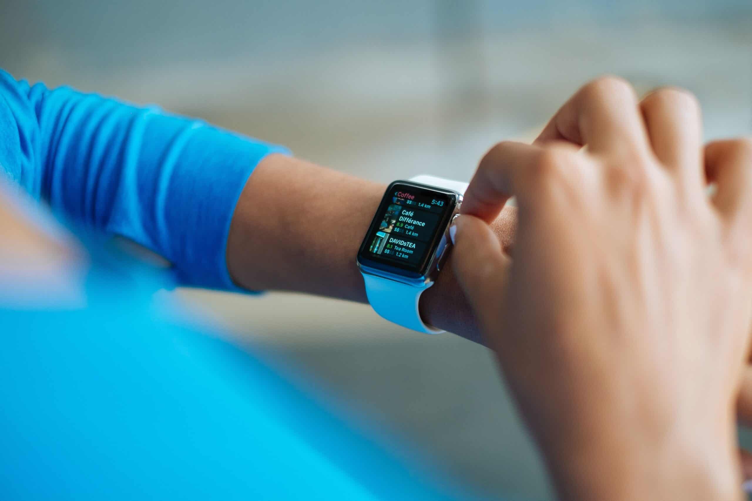 Person mit blauem Oberteil schaut auf eine Apple Watch am Handgelenk, um Wearable-Daten wie HRV und Aktivitätswerte im Alltag abzulesen und zu deuten.